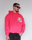 North Bioko Club Peach Hoodie in Hibiscus Pink worn by model, front view showing chest graphic and oversized fit